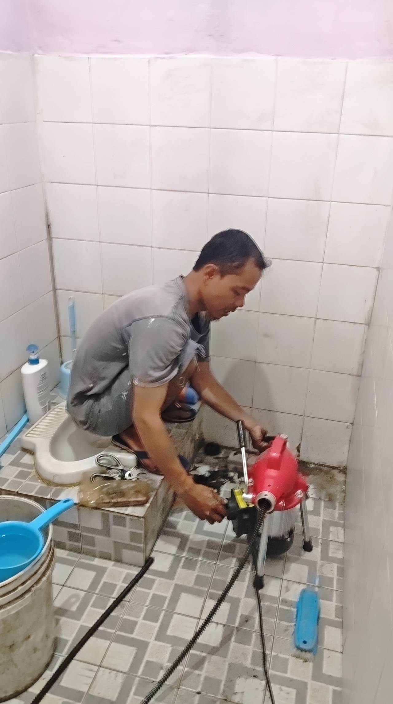 Teknisi melancarkan kloset jongkok mampet dengan mesin spiral di kamar mandi