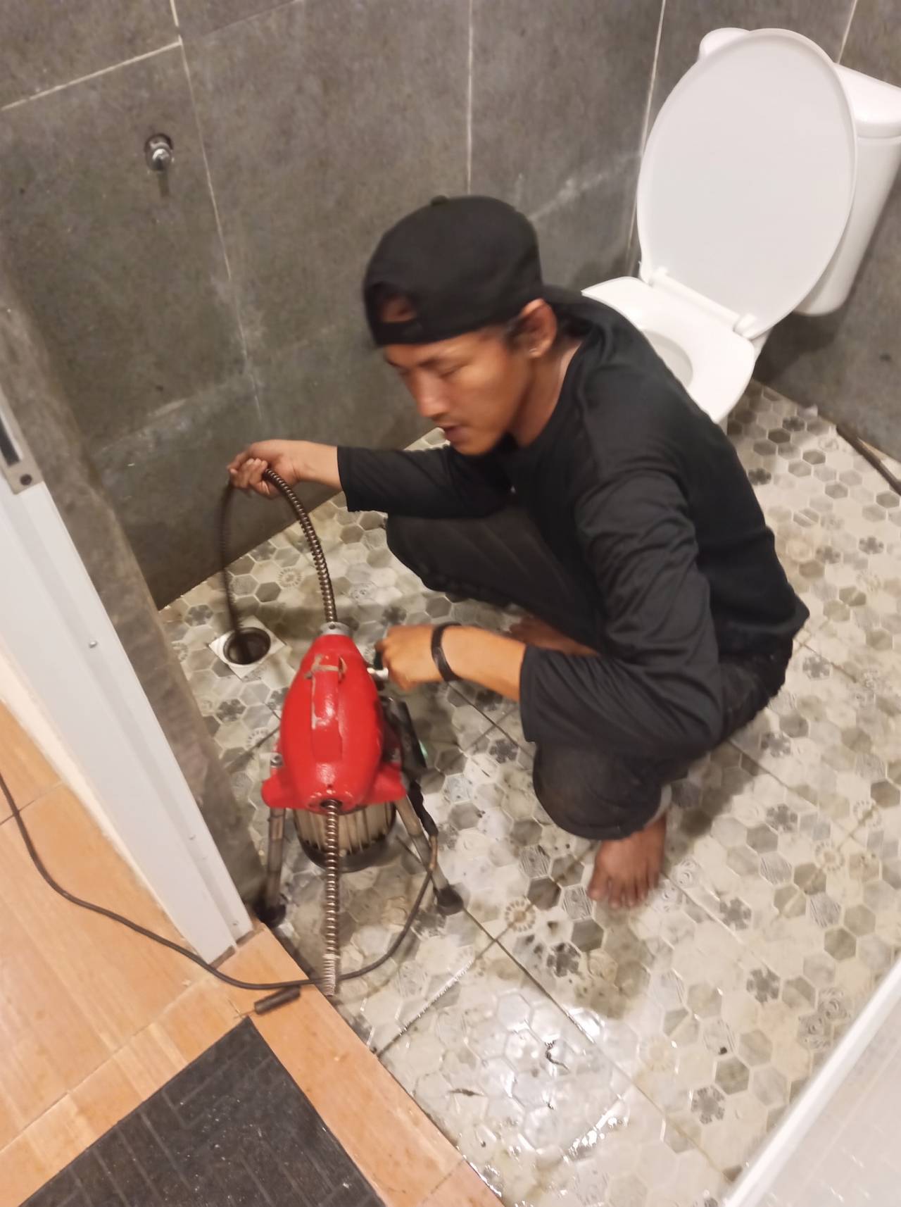 Teknisi melancarkan floor drain kamar mandi di samping kloset duduk